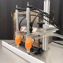 Load image into Gallery viewer, Dual nozzles on EZ Adjust Nozzle Arm in front of the FG-200 benchtop bottle filling machine on a stainless steel table